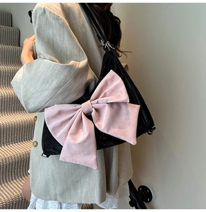Detail of a black shoulder bag with a large pink 3D bow, shown on a stylish model