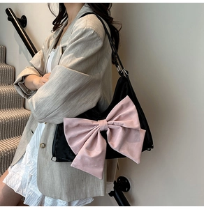 Detail of black shoulder bag featuring a large pink bow and sleek zipper closure