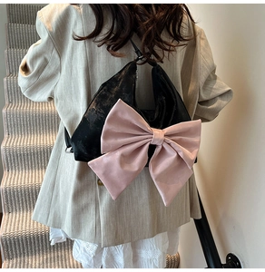 Detail of pink satin bow on a black leather shoulder bag worn by model on stairs
