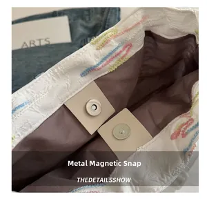 Dettaglio della chiusura magnetica in metallo e del ricamo a onde colorate sulla borsa