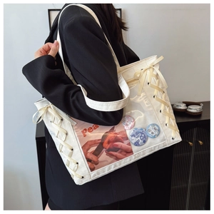 Detail of a white Ita bag with transparent window, ribbon lace-up, and anime badges