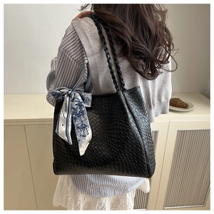 Close-up of black woven tote bag with silk scarf detail worn by a model in a casual setting