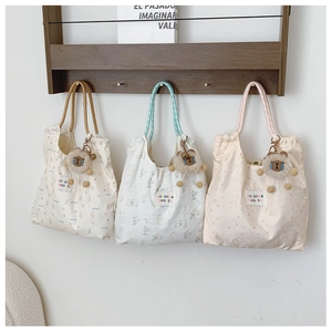 Detail of floral drawstring canvas tote bags with plush sheep charms on a rack