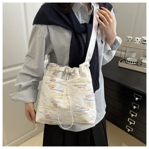 Dettaglio borsa a secchiello in tela bianca con ricami colorati e chiusura a coulisse