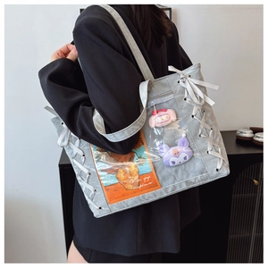 Detail of grey nylon tote bag featuring a clear PVC pocket with plush dolls and side ribbons