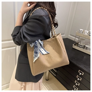 Detail of light brown tote bag featuring crocodile embossed texture and woven handle