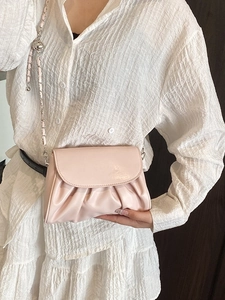 Pink pleated cloud crossbody bag with silver chain strap worn on a white textured blouse