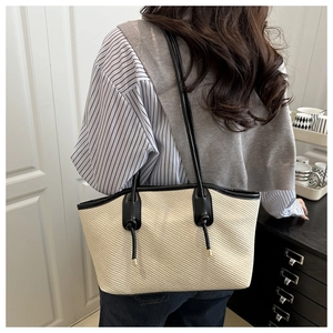 Detail of minimalist cream woven tote bag featuring black leather straps and button accents