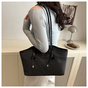 Detail of black tote bag with textured surface, knot straps and fashion text on model