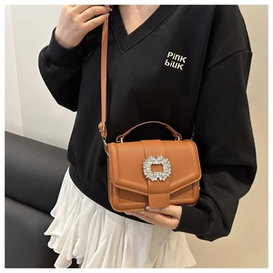 Close-up of brown litchi leather bag with a sparkling rhinestone flower buckle detail