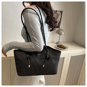 Detail of black twill woven tote bag featuring silver fashion logo and thin shoulder strap