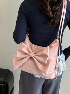 Pink crescent underarm bag with large bow and adjustable strap worn by a model