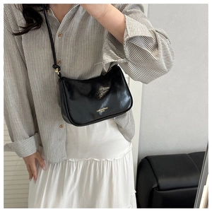 Detailed view of black glossy leather moon bag worn as a shoulder bag with gold text