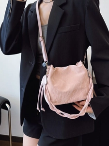 Pink pleated crossbody bag with woven handle on a black suit jacket for women