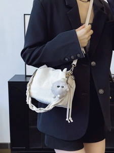 Chic beige ruched bucket bag with woven handle and plush charm on a black blazer