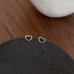 Minimalist silver hollow heart earrings displayed on a dark textured display stone