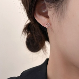 Minimalist silver heart stud earrings with linear drop design worn by a model