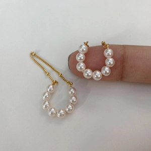 Detail of gold pearl ear cuffs with long chain fringe held on a hand for scale