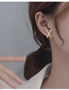 Detail of elegant gold X-shaped earring with pavé rhinestones on a female ear