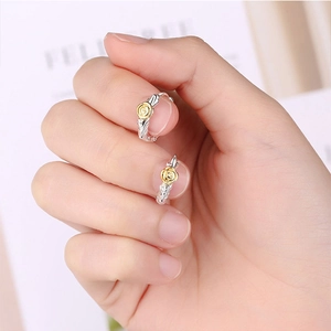 Close-up of silver hoop earrings featuring delicate golden rose details held on fingertips