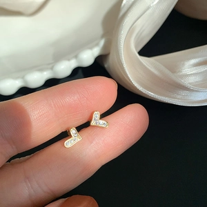 Close-up of golden V-shaped stud earrings with zircon stones held between fingers