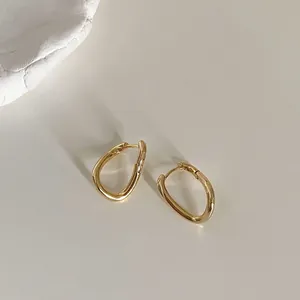Minimalist irregular wavy gold hoop earrings with fluid design on a white background