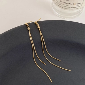 Elegant gold tassel earrings with long snake chain fringe on a minimalist display