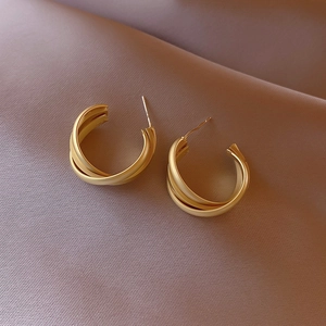 Elegant gold matte geometric twisted hoop earrings displayed on soft silk fabric