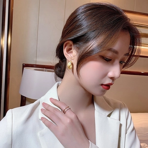 Close-up of elegant gold twisted hoop earrings and layered pavé ring on an Asian model