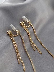 Close-up of golden long tassel clip-on earrings with soft pads on grey silk background