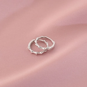 Elegant bamboo design silver hoop earrings with textured finish on pink fabric