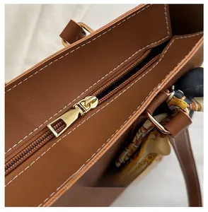 Detail of gold metal zipper and white stitching on brown leather tote bag with silk scarf