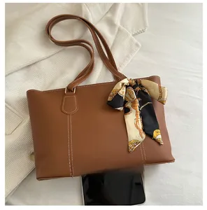 Brown tote bag detail with contrast stitching and silk scarf decoration next to a smartphone
