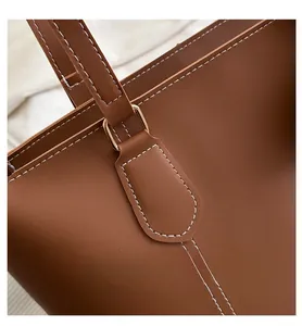 Detail of brown leather tote bag showing white contrast stitching and gold metal buckles