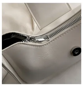 Macro detail of smooth metal zipper and magnetic buckle on white leather handbag