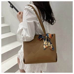 Braune Shopper-Tasche aus Leder mit modischem Seidenschal an einer Wendeltreppe