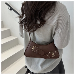 Detail of dark brown crescent bag with gold buckle accents on a striped shirt