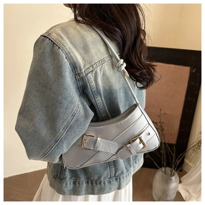 Detail of light blue leather underarm bag with metal buckles on vintage denim jacket