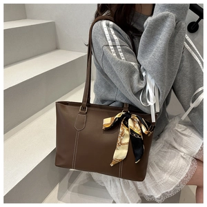 Detail of dark brown leather tote bag featuring white stitching and floral scarf decor