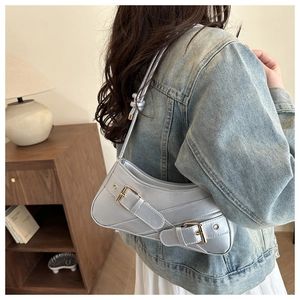 Close-up of a blue saddle shoulder bag with silver buckles in a lifestyle setting