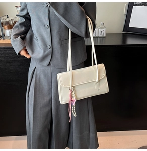 Detail of cream white leather shoulder bag with pink tassel and flap design