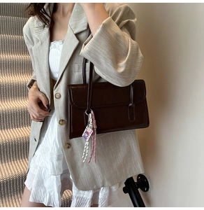 Detail of dark brown leather underarm bag with a cute cartoon charm and slim handles