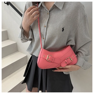 Close-up of pink crescent underarm bag with metal buckles on a model in a casual setting