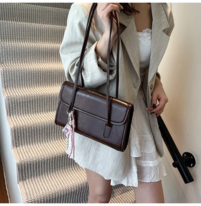 Detail of dark brown glossy underarm bag with cute pink charm on stylish white dress