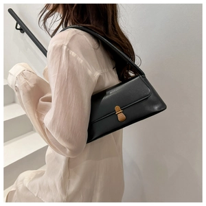 Detail view of a black minimalist baguette bag with golden buckle on a shoulder