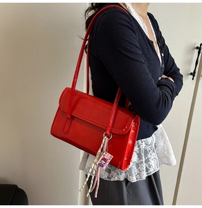 Detailed side view of a red patent leather underarm bag with decorative cartoon charm