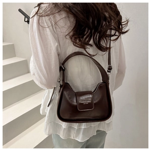 Dark brown glossy leather baguette bag worn by a model on a minimalist white staircase