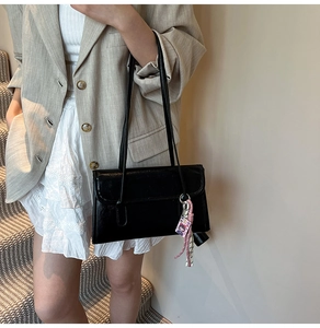 Detail of black rectangular shoulder bag with glossy leather finish and pink woven charm