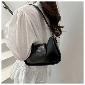 Detail of black glossy leather shoulder bag with white fashion text on minimalist stairs