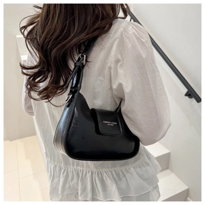 Close-up of black glossy leather baguette bag with silver hardware on a shoulder